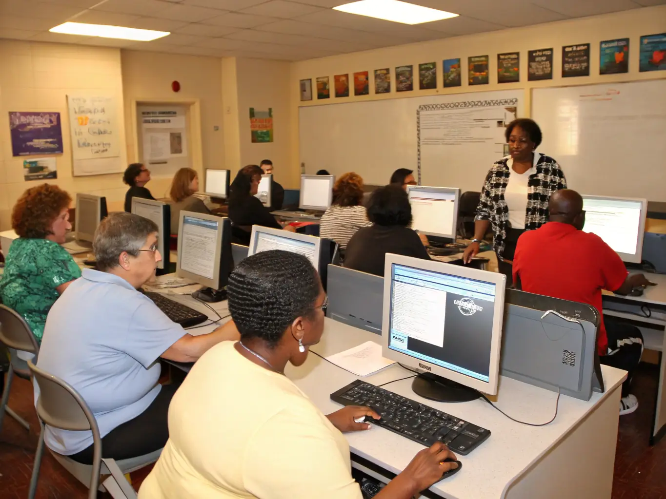 A diverse group of adults attending a computer literacy class at the association's facility, learning essential digital skills to enhance their employability and access online resources.